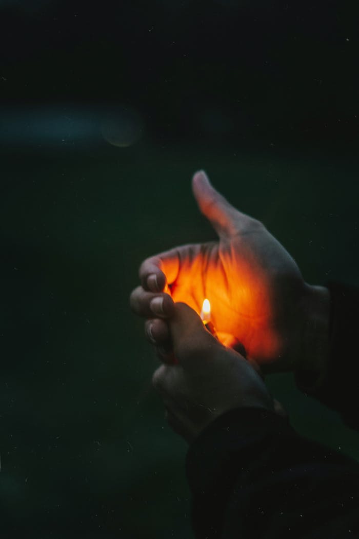 A close-up of hands cupping a lighter flame in the dark, creating a warm glow.